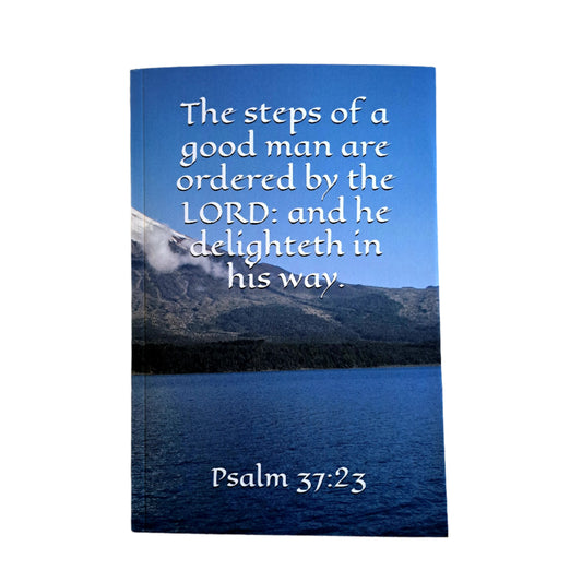 Book with Psalm 37:23 text on a mountain and lake background, placed on a white background.